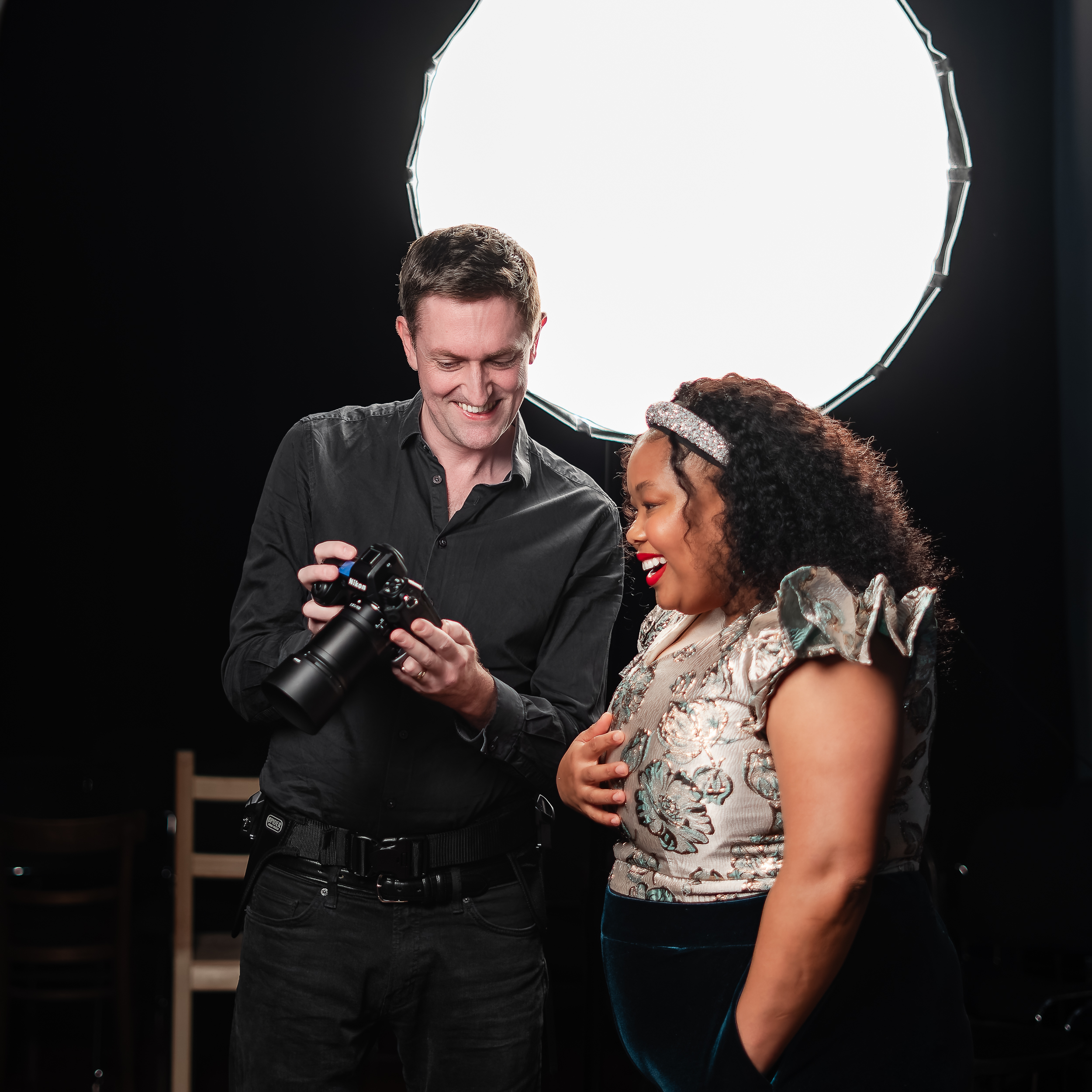 Julian Guidera showing a young singer the images on his camera that he has just taken. Backdrop of black with large white circle top right 