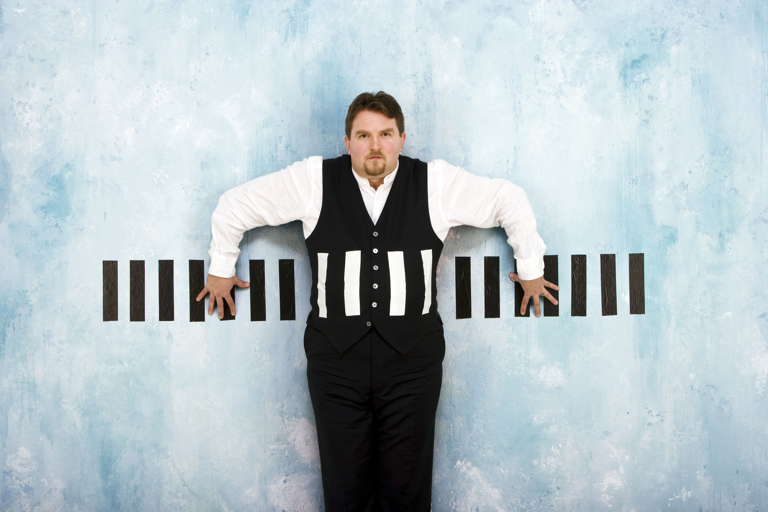 Robert Howarth standing with a piano stretched horizontally across his body.